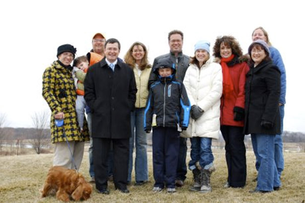 A group of supporters in winter coats, with a small dog, standing together in an open field