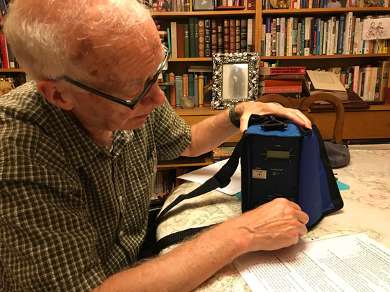A man in glasses at a table opens a blue carrying case holding a handheld air monitor