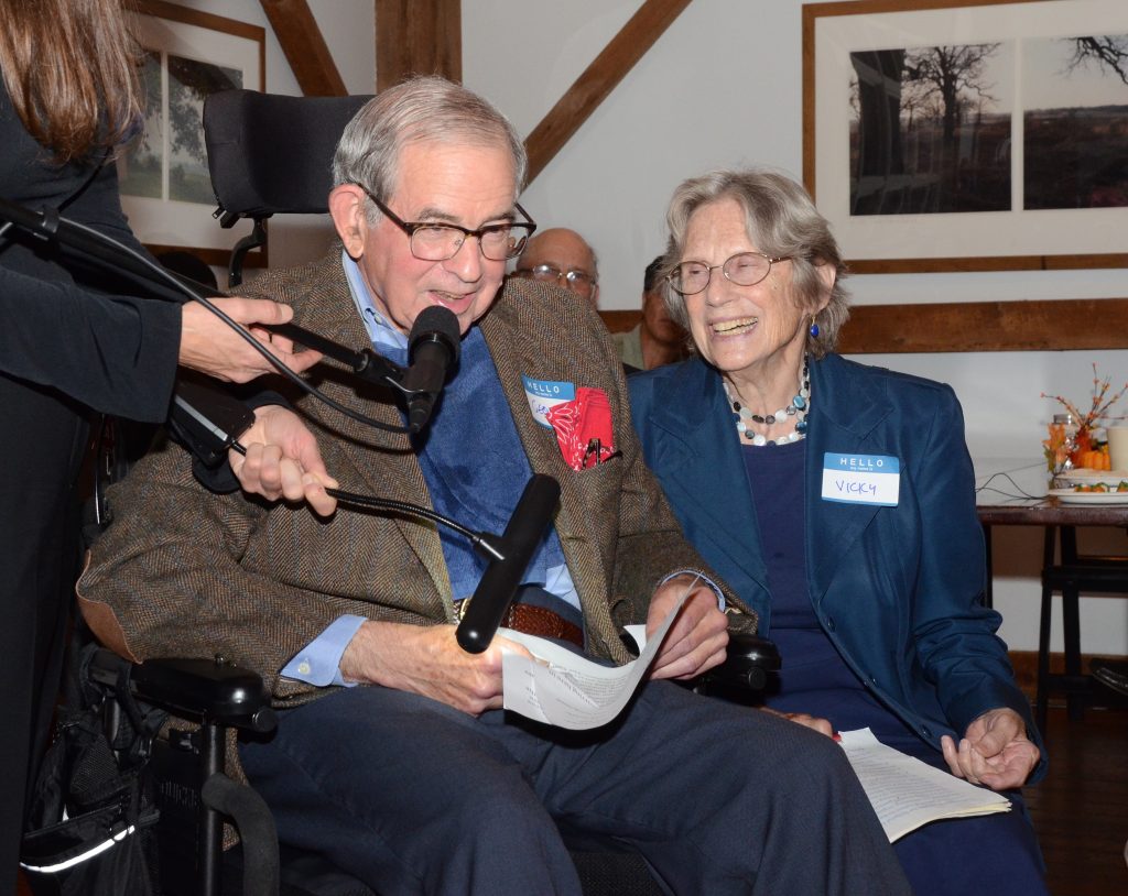 George Ranney, seated, speaks into a microphone while accepting a lifetime achievement award, with Vicky Ranney smiling beside him
